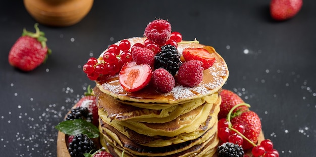 Una pila di frittelle con frutta fresca versata con sciroppo su sfondo nero