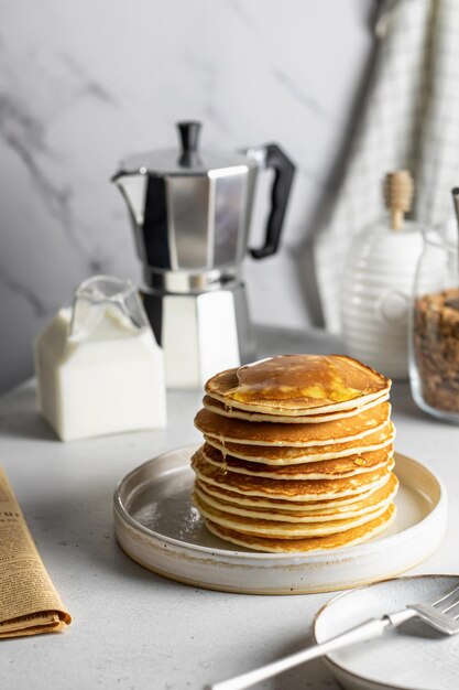 Stack of pancakes with honey coffee milk on white kitchen table Morning breakfast concept