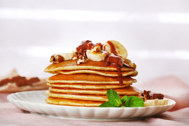 Stack of pancakes with mint, walnuts, chocolate and slices of banana on table with fabric