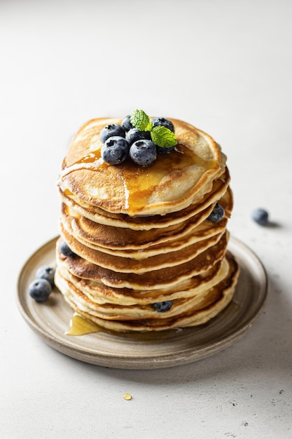 Stack of pancakes with syrup and blueberry on white textured background