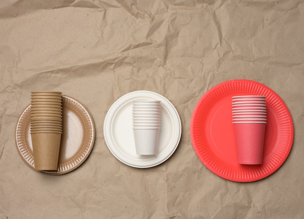 Stack of paper cups and round plates on a brown paper background. Plastic rejection concept, zero waste