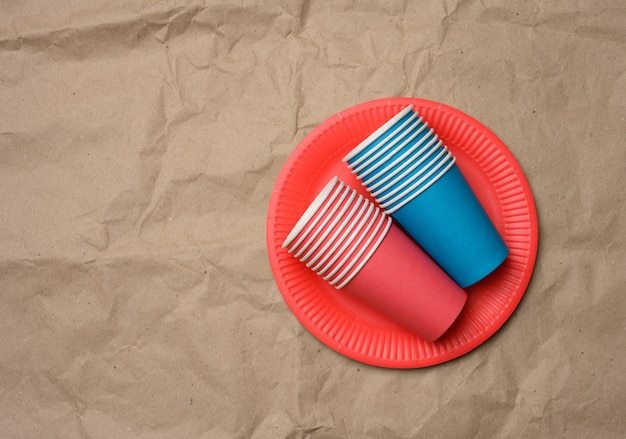 Stack of paper cups and round plates on a brown paper, top view