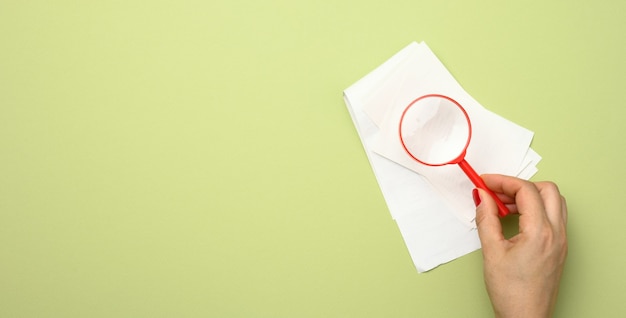 Stack of paper sales receipts and hand with a red plastic magnifying glass