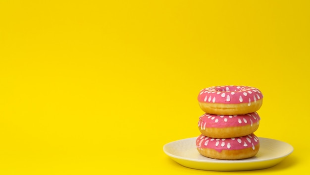 Stack of pink donuts with icing on a yellow background, copy space