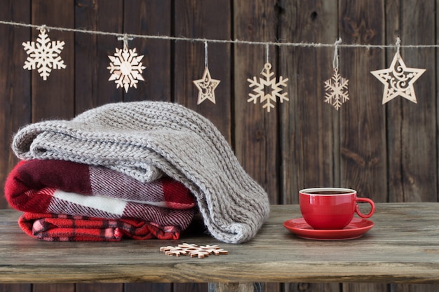 Foto pila di plaid, tazza di tè e decorazioni natalizie su fondo in legno