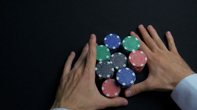 Stack of poker chips and two hands on table closeup of poker chips in stacks on green felt card