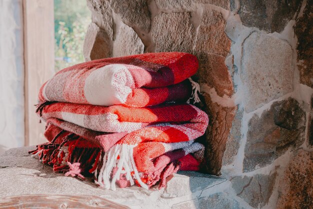 A stack of red checkered wool blankets lays down on a stone\
surface clothes cozy home vintage winter furniture heat order soft\
hobby interior autumn no people