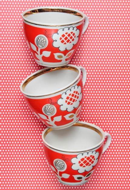 Stack of retro cups with red patterns on tablecloth whith polka dots