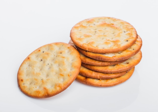 Pila di cracker salati croccanti organici rotondi su fondo bianco.