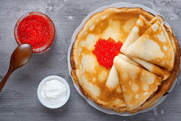 Stack of russian thin pancakes blini with red caviar and fresh sour cream