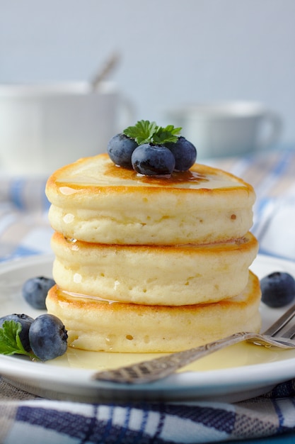 A stack of scotch pancakes with with honey and blueberries on a breakfast table