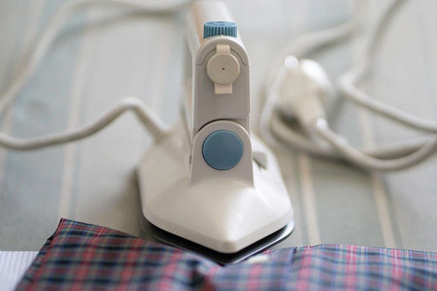 Stack of shirts and electric iron on ironing board table indoor at home Household concept