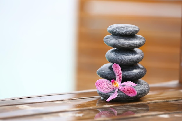 Stack of spa stones with pink orchid on wooden wet bridge