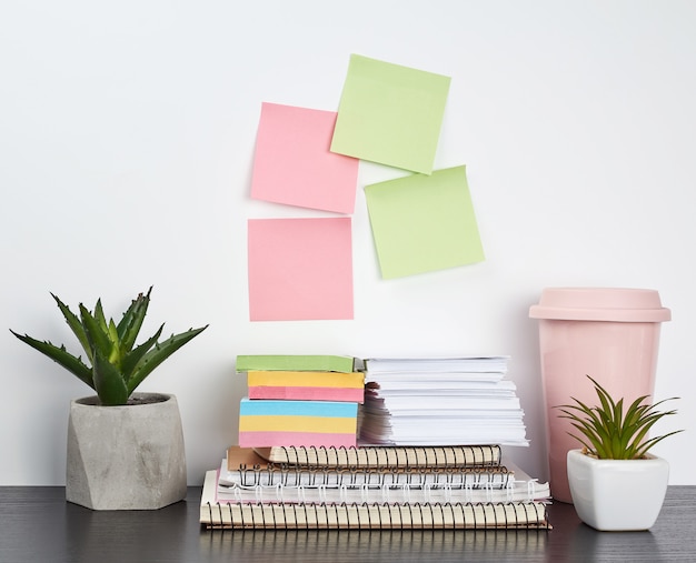 Photo stack of spiral notebooks and colored stickers, next to a ceramic pot with a flower