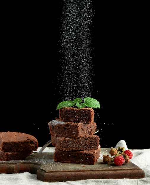 Stack of square baked brownie chocolate cake slices sprinkled with white sugar