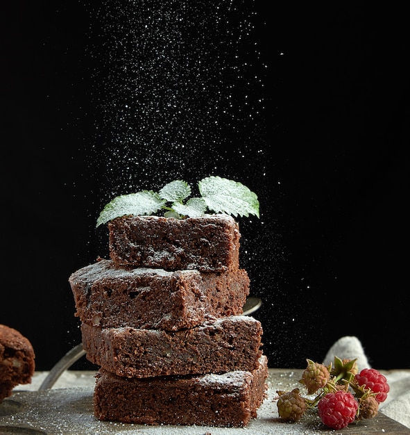 Stack of square baked brownie chocolate cake slices sprinkled with white sugar