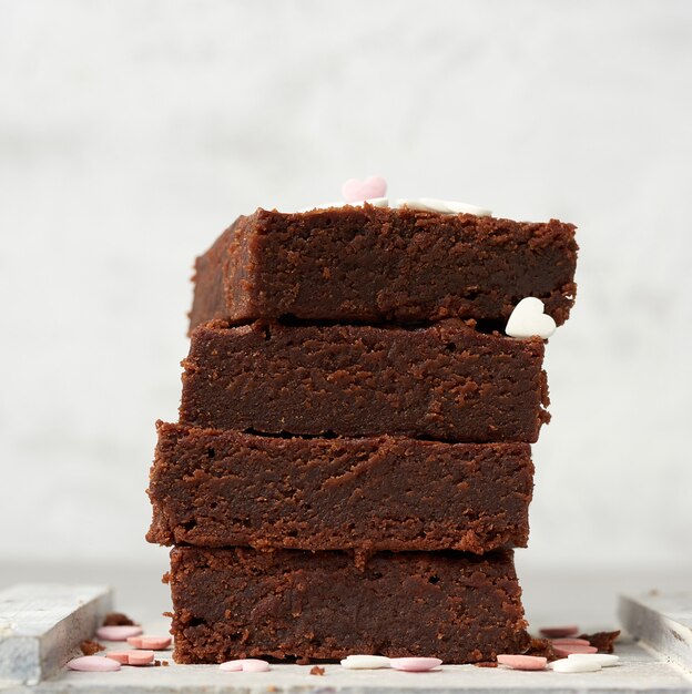 Stack of square baked brownie chocolate cake slices on a white background