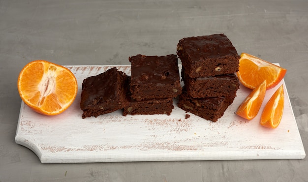 Stack of square baked slices of brownie chocolate cake with walnuts on a white wooden board