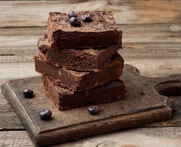 Stack of square baked slices of brownie chocolate cake with walnuts on a wooden surface. Cooked homemade food