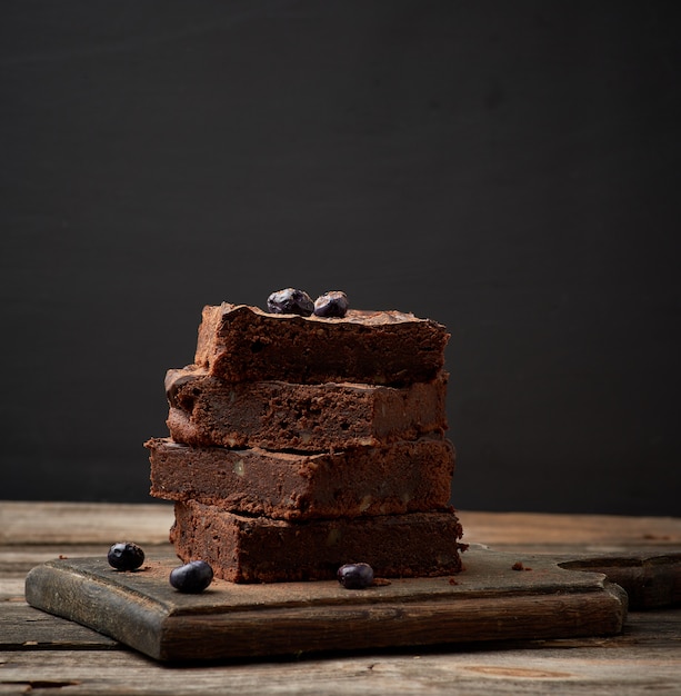 木製の表面にクルミとブラウニーチョコレートケーキの正方形の焼きスライスのスタック