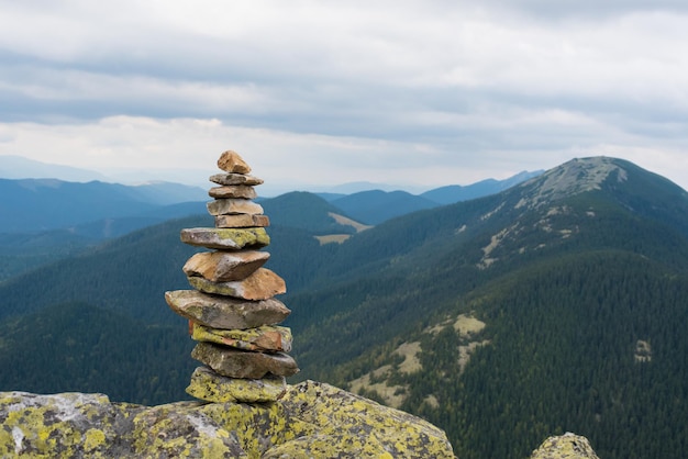 숲으로 덮인 산의 배경에 산 꼭대기에 이끼로 덮인 돌 더미. 균형과 조화의 개념입니다. 선 돌의 스택입니다. 팀워크 균형 개념