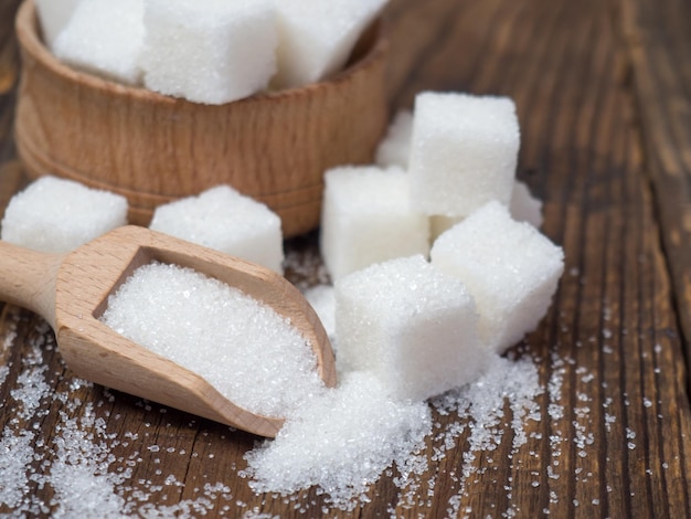 Stack of sugar cubes and granulated sugar in a wooden scoop