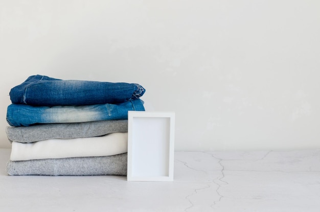 Stack of sweaters and blue jeans on grey background