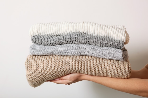 A stack of sweaters in female hands on a colored background warm clothes