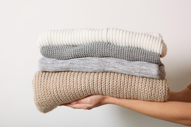 a stack of sweaters in female hands on a colored background warm clothes