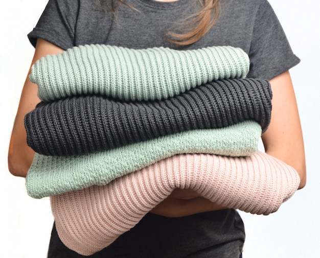 A stack of sweaters in female hands isolated on white background.