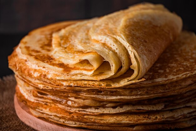 A stack of thin pancakes on a dark wooden background close up A traditional dish of crepes