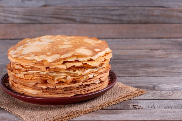 Stack of thin pancakes in a plate on a wooden table