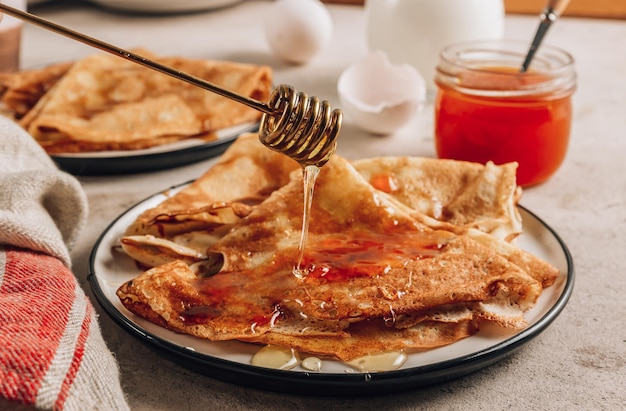 Stack of thin pancakes traditional for Russian pancake week Homemade crepes with sea buckthorn jam and milk for breakfast Selective focus