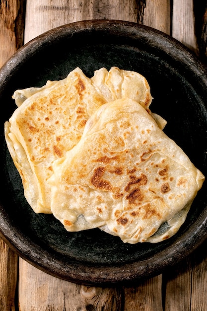Stack of traditional indian homemade fried roti flatbread in old ceramic dish over old wooden background Top view