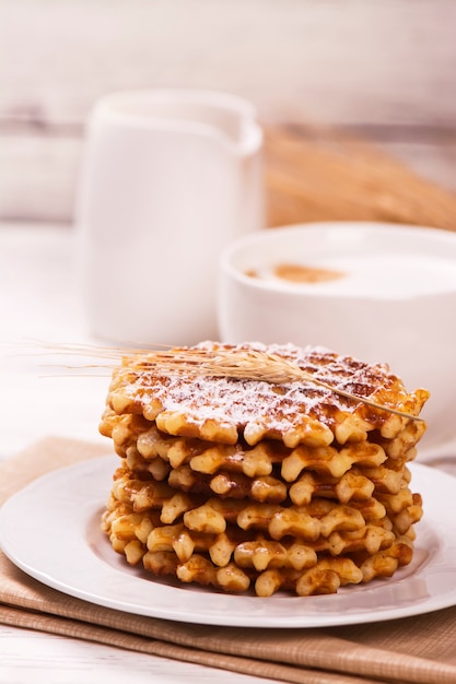 Stack van dikke Belgische wafels met suikerpoeder en kopje cappuccino koffie.