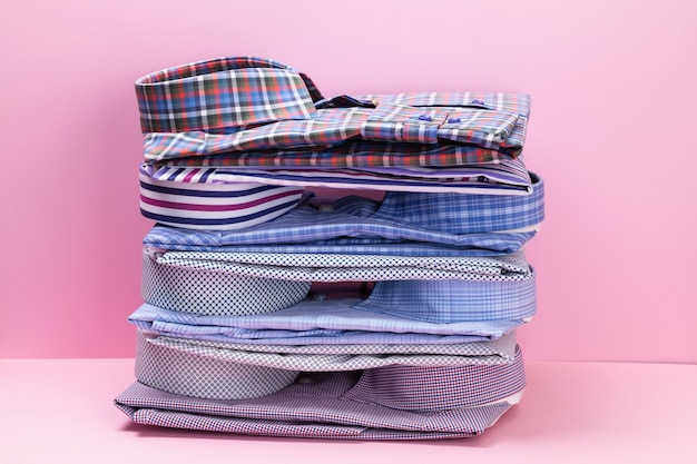 Photo stack of various folded mens shirts on pink background