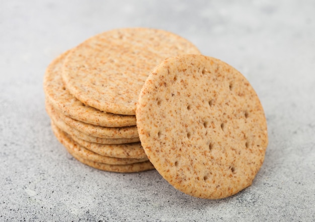 Stack of various organic crispy wheat crackers with sesame and salt on light background.