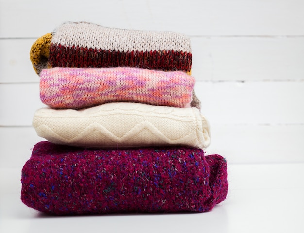 Stack of various woolen sweaters in white wall