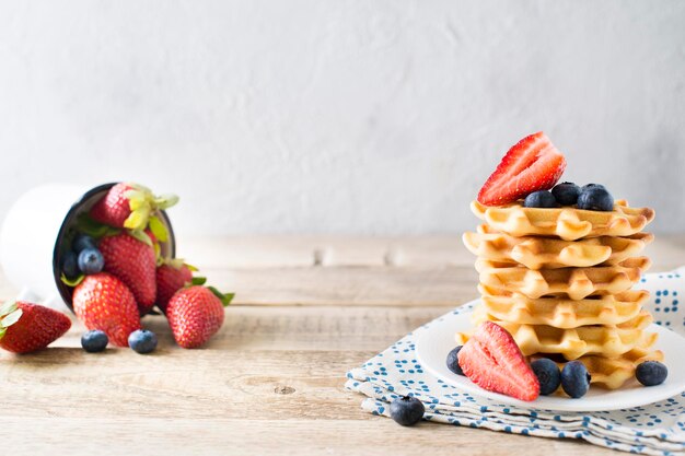 Stack of waffles with blueberries and strawberries on wooden background copy space