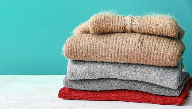 Stack of warm clothes on table against color background