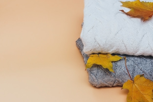 Pila di maglioni lavorati a maglia caldi con il fondo beige di concetto di autunno delle foglie di autunno gialle