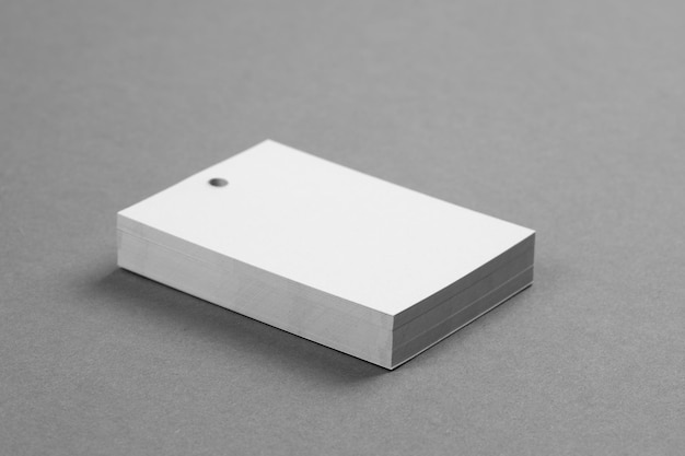 Stack of white cardboard brand label tags for clothes with\
little hole in top part of each placed exactly on each other on\
dark gray background tag mock up copy space