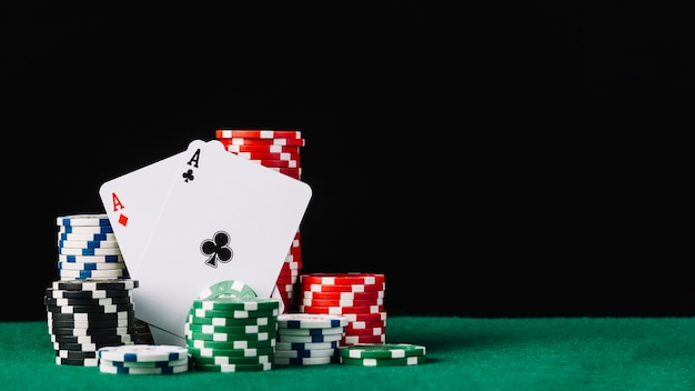 Stack of white; green; black and red casino chips with two aces on poker table