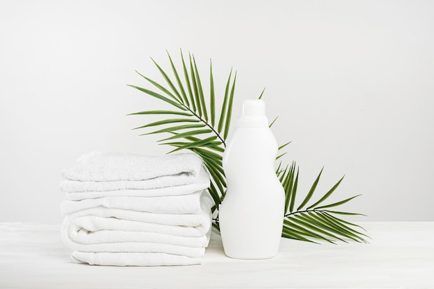 Photo a stack of white linen and a bottle of white palm-leafed laundry detergent or fabric softener. tropical laundry day mockup.