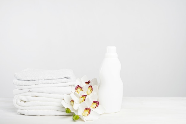 Stack of white linen, washing gel and fabric softener on a white table with orchid flowers. Mockup laundry day in a tropical hotel with copy space.