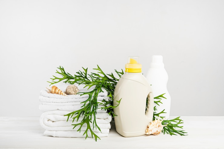 Photo a stack of white linen, washing gel and fabric softener on a white table with seaweed and seashells. mockup laundry day in a tropical hotel. liquid detergent bottle.