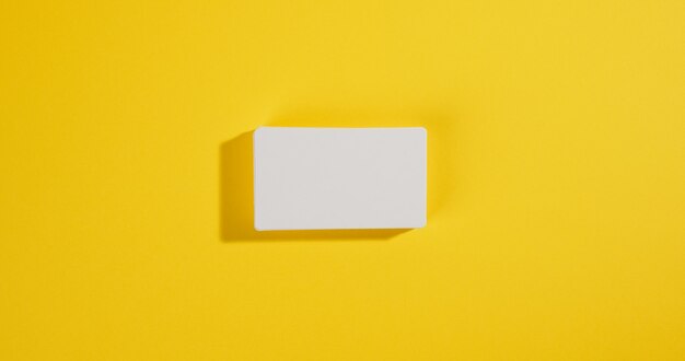 A stack of white rectangular business cards on a yellow surface, company branding, address. View from above, flat lay