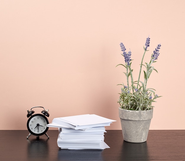 Stack of white square note papers, a ceramic pot of lavender and an alarm clock 