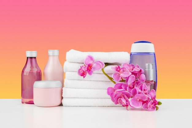 Stack of white towels and bottles of skincare on white table