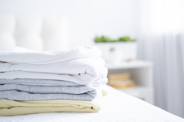 Stack of women colorful sweatshirts, hoodies in pastel colors on white bed. Seasonal shopping, laundry, vacation concept.